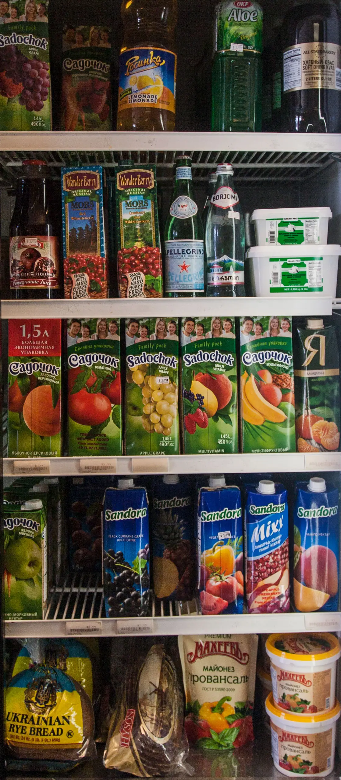 Refrigerated shelves at Aleksey's Market with European juices, mineral water, rye bread, and mayonnaise.