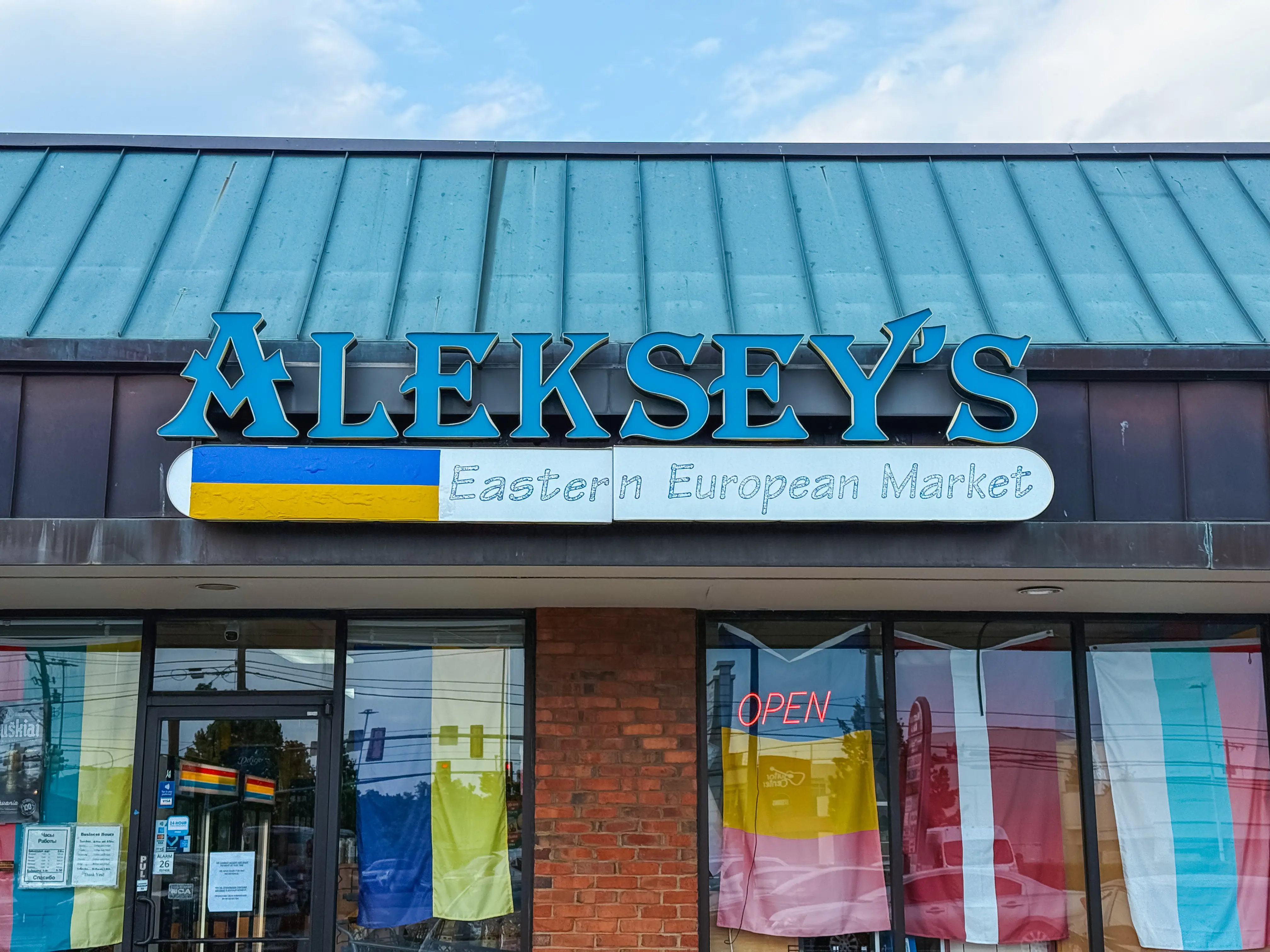 Aleksey's Market storefront sign in Nashville with an open sign and flags in the windows.